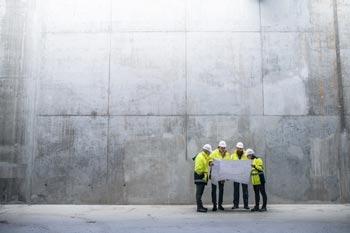 Cement engineers studying plans in front of a large concrete wall